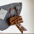 Braune glänzende Lederhandtasche mit großer Nietenschleife und schmalen Doppelgriffen - Braun