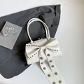 Witte lakslederen handtas met strik en zilveren studs op een grijze ondergrond - Wit