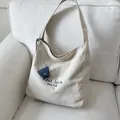 Minimalist beige canvas tote bag with contrast blue leather charm on a white sofa - Off White