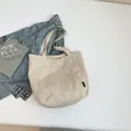 Minimalist off-white nylon tote bag with front pocket and small black brand label tag - Beige