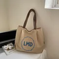 Khaki Canvas-Einkaufstasche mit braunen Riemen und blauer Stickerei auf dem Schreibtisch - Khaki