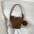 Minimalistische dunkelbraune Beuteltasche mit langen Trägern und rundem Taschenanhänger - Braun