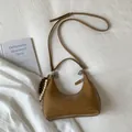 Detail of a brown woven underarm bag featuring a beaded charm on a soft fabric background - Khaki
