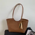 Dettaglio di una borsa tote intrecciata marrone con una nappa di perline decorativa - Marrone con ciondolo