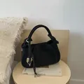 Black suede hobo bag with a knotted handle and heart pendant on a wooden stool - Black