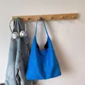 Close-up of a royal blue suede tote bag hanging on a wooden wall hook with headphones - Blue