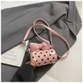 Pink polka dot cylinder bag with bow detail on a stylish grey blazer background - Pink