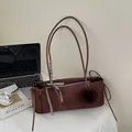 Dunkelbraune Wildleder Schultertasche mit Karoschleife und Plüschball in Lifestyle-Szene - Braun mit Anhänger