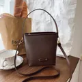 Borsa a secchiello marrone scuro con trama a grana e tracolla su superficie in legno - Marrone senza ciondoli