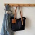 Minimalistische zwarte nylon draagtas met bruine leren riemen aan een houten rekje - Zwart en Bruin