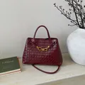 Close-up of dark red woven leather bag with signature gold knot buckle and long strap - Red