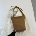 Detailansicht der braunen Wildleder-Beuteltasche mit Metallfüßen auf einem Blazer - Braun