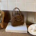 Dettaglio mini borsa in camoscio marrone scuro con fiocco decorativo posata su libri - Marrone