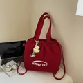 Red nylon drawstring tote bag with white logo and yellow plush charm on desk - With Pendant / Red