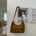 Detail der Wildleder-Schultertasche mit Kontrastnähten und Boho-Quasten-Anhänger - Braun
