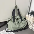 Sage green nylon travel bag with drawstring pocket and black handles on a grey background - Green