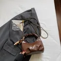 Brown pleated dumpling bag with gold chain strap and tassel charm on grey suit background - Brown