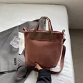 Bolso tote de ante marrón con asas de cuero y correa tejida sobre una cama blanca - Marrón