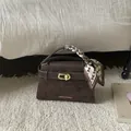 Close-up of deep brown leather handbag featuring a golden clasp and decorative silk scarf - Brown