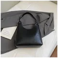 Minimalist black leather hobo bag with gold eyelet detail on a grey suit background - Black without Pendant