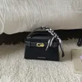 Close-up of black suede handbag with gold turn-lock and decorative silk scarf handle - Black