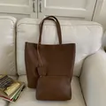 Dettaglio del set borsa a secchiello in pelle marrone con pochette abbinata su un divano - Set Borsa e Pochette / Marrone