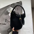 Minimalist black suede bucket bag with gold buckle and adjustable strap in hand - Black
