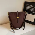 Braune gefrostete Beuteltasche mit Goldnieten und Lederriemen in minimalistischer Szene - Kaffeebraun