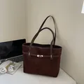 Bolso tote de ante marrón oscuro con cierre giratorio dorado en un escritorio minimalista - Marrón