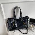 Glossy black leather tote bag with braided handles and golden zippers on a desk - Black