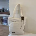 Detail of cream quilted tote bag featuring a brown leather logo and dark bow pendant - With Pendant / White
