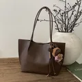 Vue latérale d'un sac cabas en cuir marron avec un charme ours et des fines bandoulières - Avec Pendentif / Marron