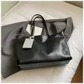 Minimalist black tote bag in textured leather with sleek shoulder straps on white bedding - Black