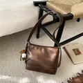 Détail du sac bandoulière bronze métallisé avec pendentif baseball sur chaise vintage - Avec Pendentif / Marron