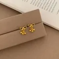 Golden bow stud earrings with three small solid sphere drops on a brown display card - Golden Bow With Beads Pendant
