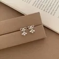 Silver bow stud earrings with small metal ball pendants on a warm brown display - Silver Bow With Beads Pendant