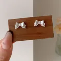 Elegante silberne Schleifen-Ohrstecker mit feiner Textur auf Holz-Display-Ständer - Silberne Schleife