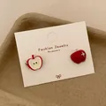 Weihnachtliche rote Apfel-Ohrstecker mit Goldfinish auf weißer Schmuckkarte - Asymmetrischer Emaille Roter Apfel Stil