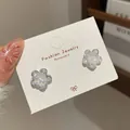 Elegante Blumenohrstecker mit schillernden Blütenblättern und weißen Perlen auf Displaykarte - Irisierende kleine Blume