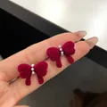 Red flocked bow earrings with three small pearls shown on a hand for scale - Double Heart Bowknot (RV30)