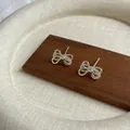 Silver bow knot earrings with textured finish and long tassels on dark wooden stand - Twisted Bow