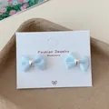 Light blue ribbon bow stud earrings with silver heart detail on jewelry card - Blue Heart Bowtie