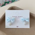 Light blue fabric bow earrings with pearl clusters on a fashion jewelry display card - Blue Artificial Pearl Bowtie