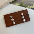 Elegante silberne Dreifach-Herzohrringe auf einem dunklen Schmuckständer aus Holz - Dreifach-Herz-Stil (UC2) / Silber