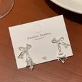 Silver bow earrings with asymmetrical Christmas tree and bell pendants in zircons - Christmas Bell