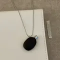 Retro black pebble pendant necklace with silver chain on a white notebook background - Black Oval Necklace