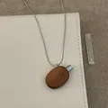 Close-up of a vintage wood perfume bottle pendant on a silver snake chain over a notebook - Coffee Oval Necklace