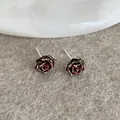 Macro detail of dark red rose earrings with gold edges on a gray velvet surface - Black Red Rose