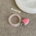 Detalle de un dije de fresa rosa en un coletero en espiral mate sobre una textura de fieltro - Estilo 10 Coletero de Fresa con Cordón de Teléfono