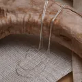 Détail de chaînes multicouches argentées suspendues sur un support en bois naturel rustique - Style Superposé à Trois Rangs / Argent